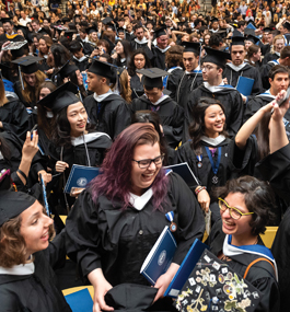 Students standing in caps and gowns smile and talk at Commencement